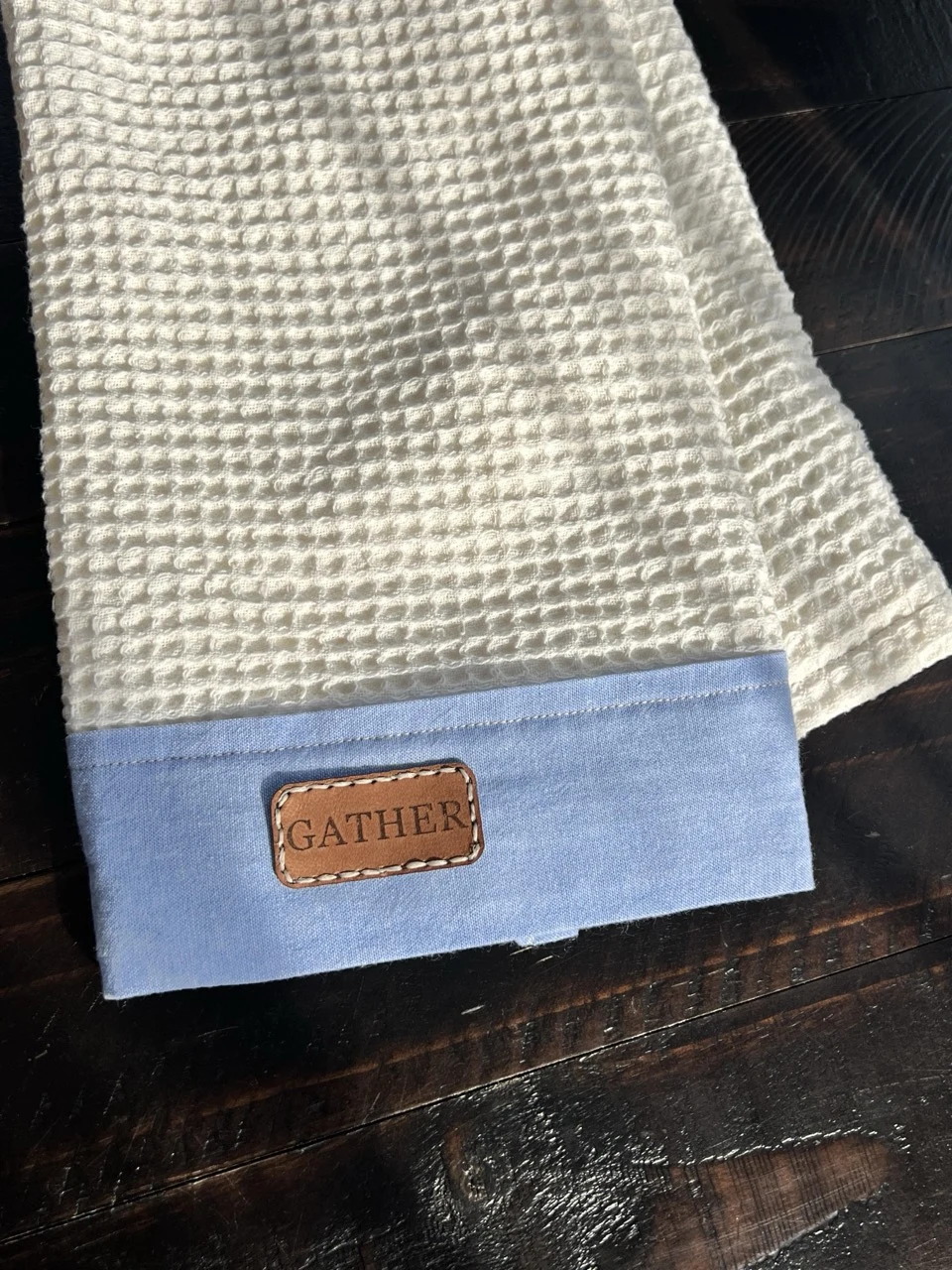 Cream waffle-textured tea towel with a blue chambray border and Gather patch